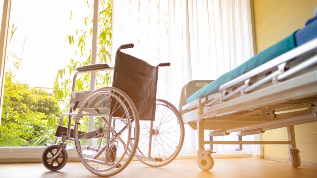 Manual wheelchair parked beside a hospital bed in a sunlit recovery room.
